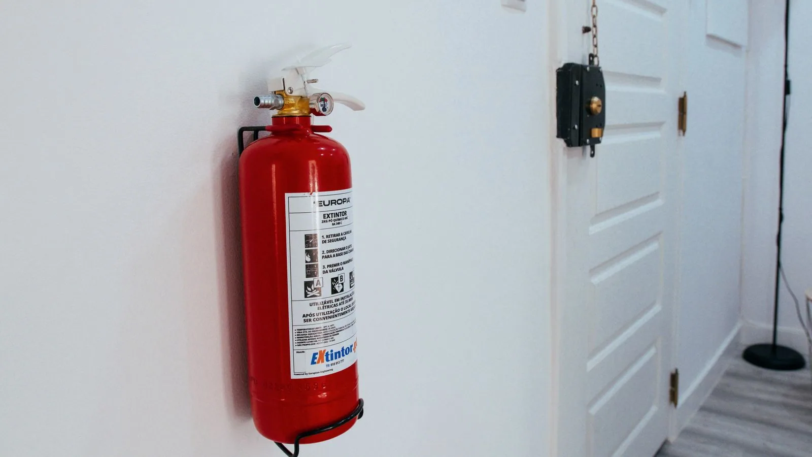 Photographie : un extincteur rouge fixé au mur d'un atelier, à hauteur de main près de la porte